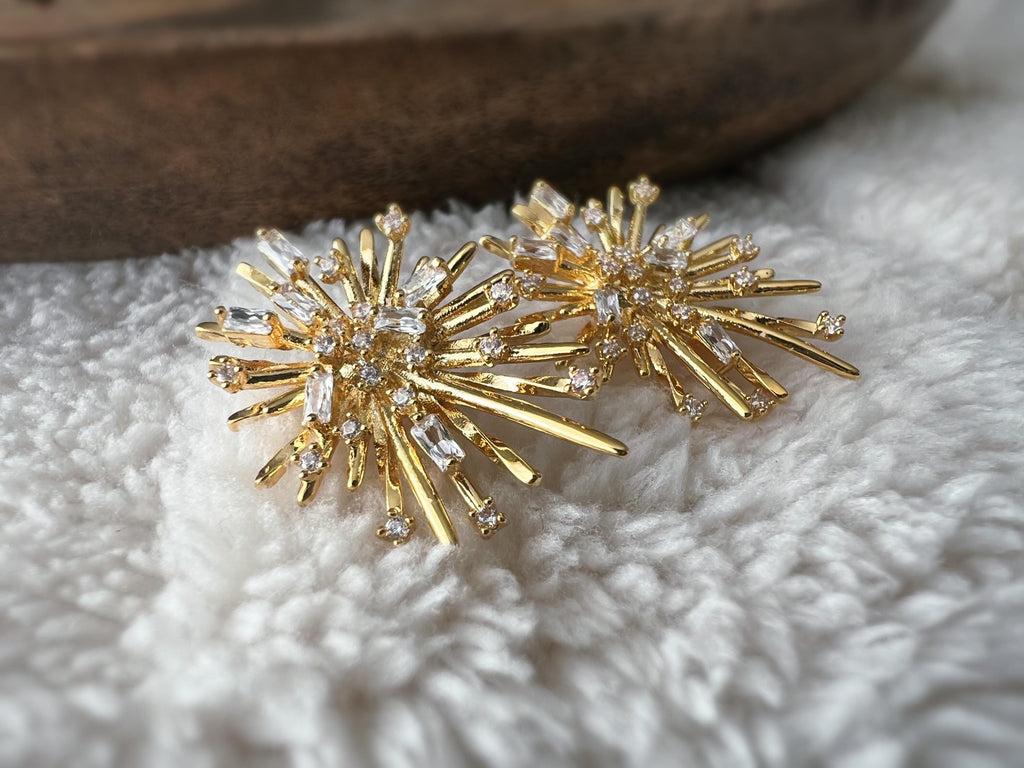 Clips d'oreilles dorés en forme de rayons lumineux, sertis de cristaux étincelants. Une touche glamour idéale pour sublimer vos tenues.