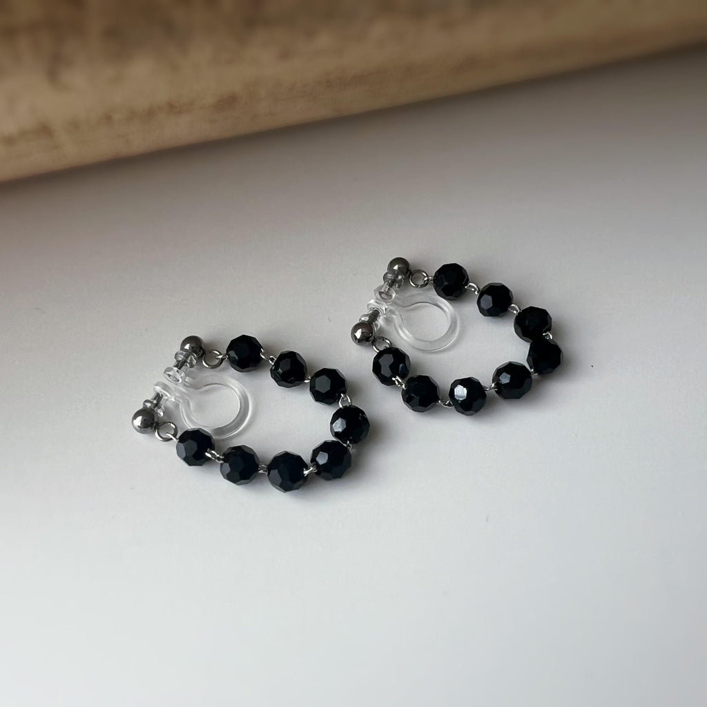 Boucles d'oreilles clips élégantes avec perles noires facettées en forme de cercle. Idéales pour un look raffiné et intemporel.