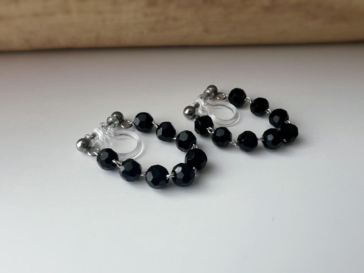 Boucles d'oreilles clips élégantes avec perles noires facettées en forme de cercle. Idéales pour un look raffiné et intemporel.