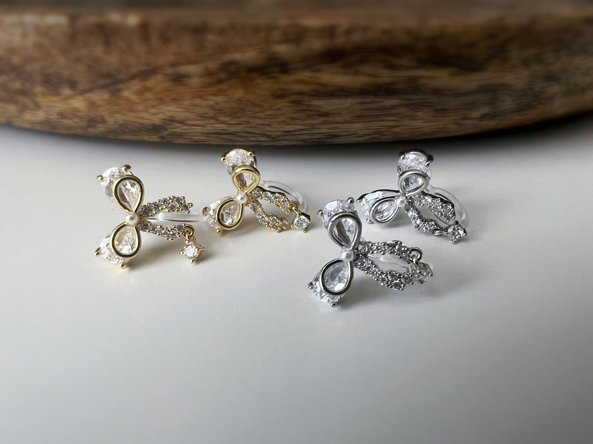 Clips d’oreilles papillon en strass, disponibles en doré et argenté. Design raffiné pour un look délicat, sans perçage.