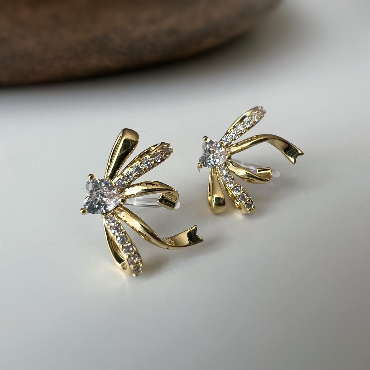 Clips d’oreilles élégants en forme de nœud scintillant Or / Argent sertis de strass étincelants. Bijou raffiné pour un style chic et féminin