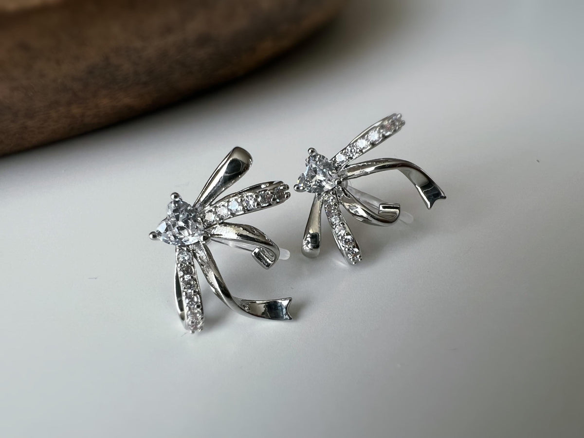 Clips d’oreilles élégants en forme de nœud scintillant Or / Argent sertis de strass étincelants. Bijou raffiné pour un style chic et féminin